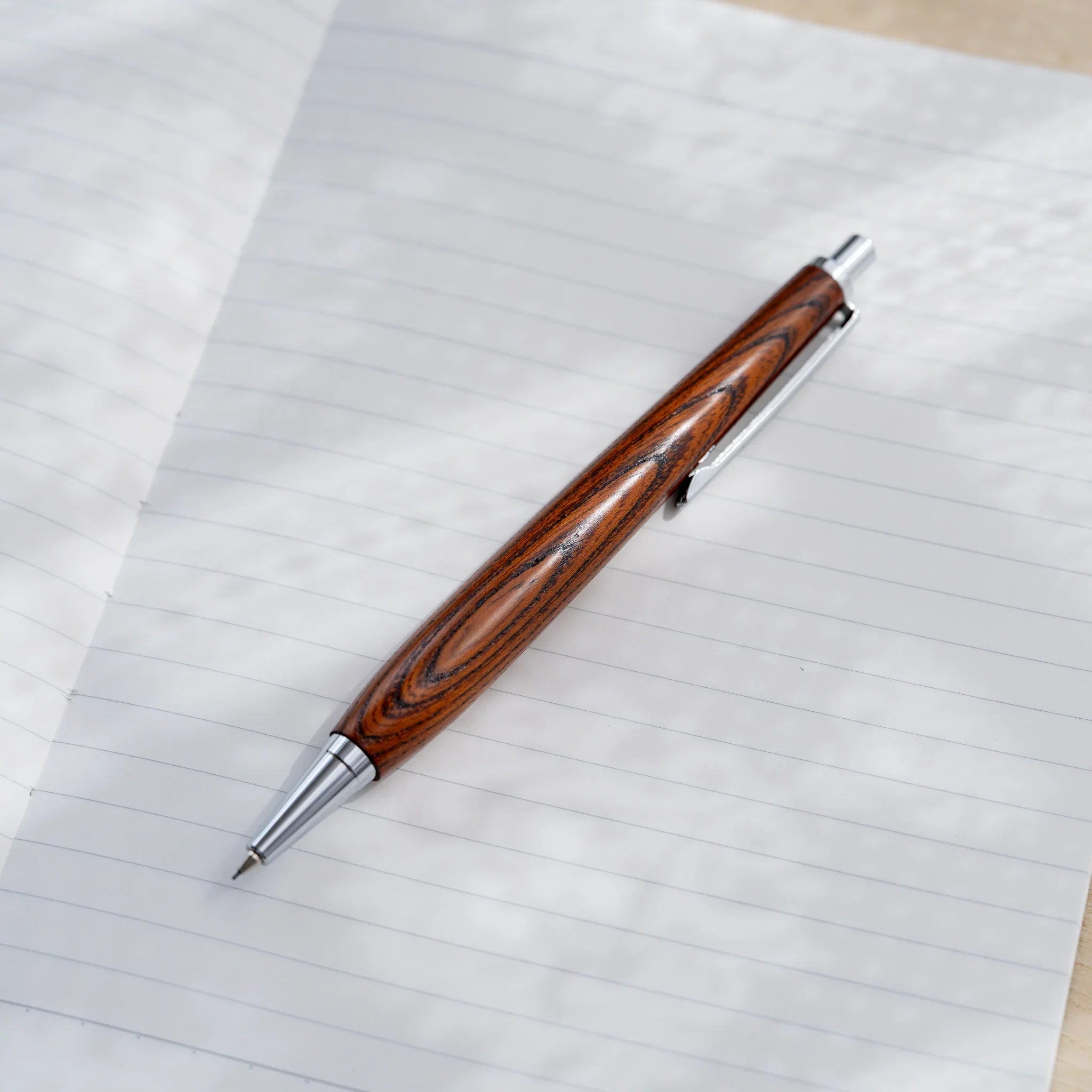 Zelkova wood urushi lacquered mechanical pencil in amber-brown on pale surface, Japanese keyaki, silver knock