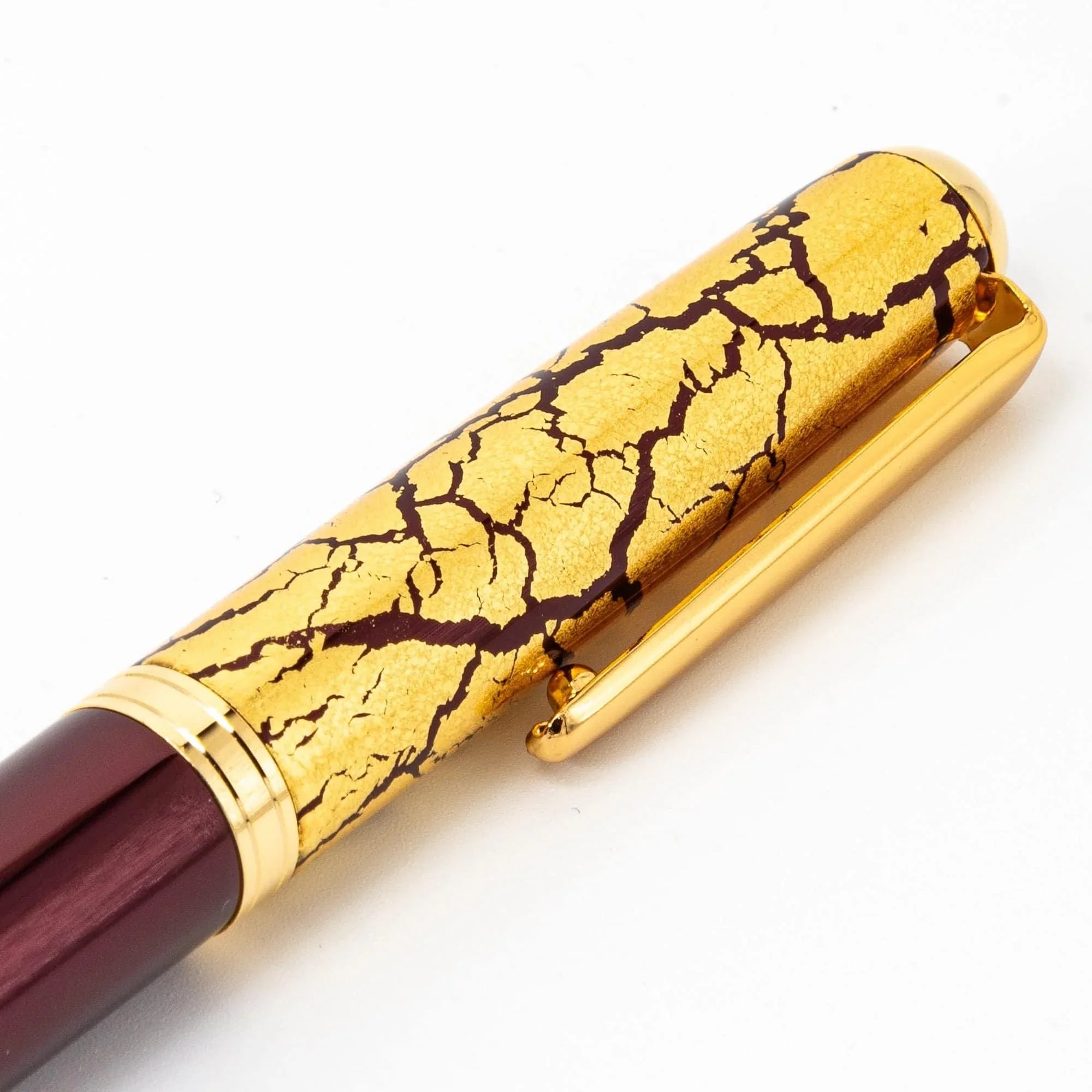 Wine red fountain pen barrel detail exhibiting fine intricate gold crackle pattern on dark lacquer finish