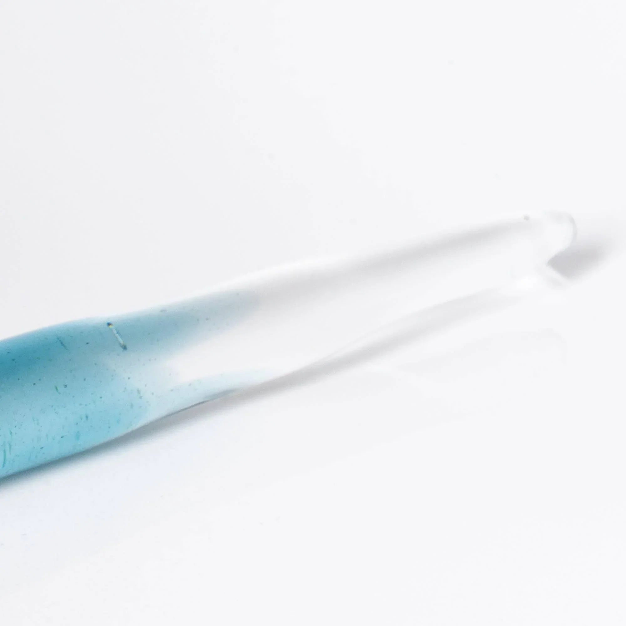 Hand-held demonstration of light blue glass dip pen positioned for calligraphy and decorative lettering work shine